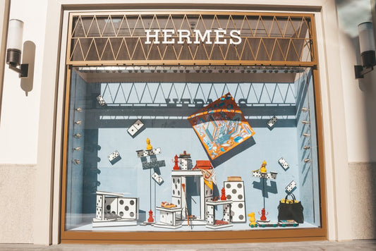 Artistic window display at a Hermes store featuring domino-themed decor and luxury items.